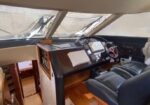 Boat cockpit interior showing a wooden dash with navigation screen, steering wheel, and black leather captain's chair.