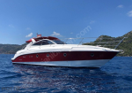 Luxurious white and burgundy motor yacht cruising on calm blue water with a hilly coastline in the background, red canopy on the upper deck.