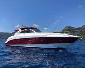 2008-beneteau-monte-carlo-37-power-9873026-20250715095011334-1 | Boat Universe Luxurious white and burgundy motor yacht cruising on calm blue water with a hilly coastline in the background, red canopy on the upper deck.
