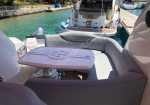 Curved outdoor seating around a pink table on a yacht deck, with turquoise water and other boats in the background.
