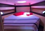 Cozy boat cabin with a double bed, striped bedding, red pillows, and porthole windows on either side.]","Interior of a yacht cabin: bed with blue-and-white striped sheets, red cushions, purple lighting."