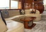 Cream leather curved sectional sofa with decorative pillows in a yacht lounge, beside glossy wood paneling and large windows awaiting tide.