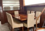 Wooden dining table with eight beige upholstered chairs in a yacht-style cabin dining area.