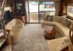 Luxurious beige leather yacht lounge with curved seating, a polished wooden coffee table, and sliding glass doors to the deck outside.
