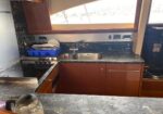 Compact yacht galley with dark marble counters, stainless sink, dish rack, and kettle on the counter