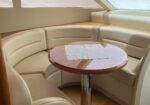 Curved beige leather seating surrounds a round wooden table with a white napkin in a boat cabin dining area.
