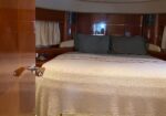 Hotel-style boat cabin with a large bed, beige textured cover, dark gray pillows, and polished wooden walls on both sides.