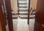 Narrow interior hallway with carpeted stairs rising ahead and a right-hand metal handrail.