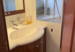 Modern bathroom vanity with white oval sink, chrome faucet, and soap dispenser; mirror cabinet above and shower visible in the background.