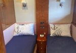 Twin bunk cabin on a ship with navy bedcovers, white anchor-pattern pillows, and a wooden nightstand between beds.