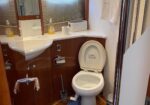 Small bathroom with a white open-toilet, sink, and wood-paneled cabinets; soap dispensers, tissue box, and roll on the counter are visible life.