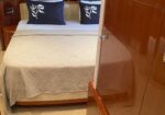 Queen bed with a beige quilt and two navy pillows featuring white floral designs, in a wood-paneled cabin surface nearby.
