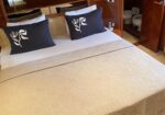 Queen bed in a wooden cabin with two navy pillows featuring white floral motifs and a beige textured quilt; bathroom door visible in the background.