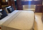Luxurious hotel-like bedroom with a large bed, beige quilted cover, and navy pillows with white leaf designs against white sheets.