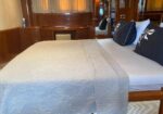 Bed with white quilt and light gray runner in a wood-paneled yacht cabin, dark blue pillows with white leaf patterns.