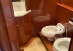 Wood-paneled bathroom with a white sink on the left and a toilet and bidet on the right; beige rug on the wooden floor.