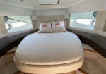 Luxury yacht cabin with a centered white bed, two coral-pattern pillows, and porthole windows along the sides.