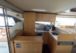 Wooden galley on a luxury boat with sink, microwave, coffee maker and cabinetry along the counter, visible deck outside.