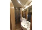 Hotel bathroom with a curved white sink, multiple mirrors, and a glass shower; a person is visible in the mirror taking a photo.