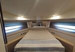 Cozy yacht cabin with a wide central bed, beige linens, and built-in side drawers under padded walls with windows on both sides.