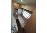Compact camper cabin with two single beds along opposite walls, built-in wooden storage and a narrow central aisle.