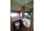Compact boat bathroom with toilet, curved sink, and large mirror; porthole window on the left.