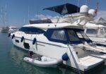 Large white motor yacht docked in a marina with a small inflatable dinghy tied at the stern.