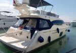 White motor yacht docked in a marina with blue canvas covers and fenders along the hull, calm water nearby (informative image).