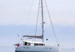 White sailing yacht on calm water with a tall mast and furled sails.