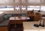 Cozy boat cabin with L‑shaped gray sofa, a wooden oval table with a fruit bowl, and a nearby galley stove.