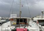 M white luxury catamaran named LARA docked in a marina, solar panels extended on the stern and other boats moored nearby under a cloudy sky.