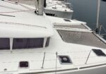 White catamaran deck with netting/trampoline area and cabin windows, moored on calm water