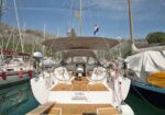 Rear view of a white sailing yacht docked in a marina, teak deck and steering wheel visible