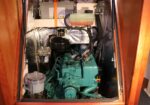 Diesel engine room of a boat with a teal-green engine, coolant reservoir, and braided hoses surrounded by insulation panels.