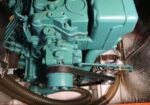 Teal-colored diesel engine with a belt-driven pulley and various hoses in a compact engine bay.