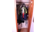 Open wooden coat closet with colorful jackets on hangers and backpacks stored at the bottom