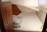 Narrow bunk bed in a small boat cabin with a striped blanket folded on top.