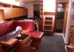 Cozy sailing yacht saloon with red leather sofa, wooden cabinets, and a small table with a white lamp.