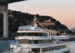 White passenger riverboat named Sultania docked by a waterfront at dusk, string lights on the deck.