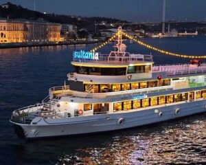 2012-turkish-boat-yard-49m-power-10046335-20251230092710783-3 | Boat Universe Nighttime view of a white, three‑deck passenger boat named 'Sultania' with string lights, on calm water with a lit city promenade in the background