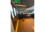 Indoor bar area with a glossy black counter, warm yellow lighting, and rows of glassware; wooden floor and exit sign near the door.
