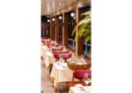 Restaurant dining area with white-tablecloth tables, red chairs, and wine glasses along a wooden wall paneling.