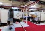 Industrial utility room with large white cylindrical tanks, exposed pipes, and red carpet runners.”