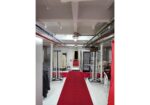 Backstage area with a red carpet runway, clothing racks, and equipment along both sides.