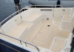 Empty boat cockpit at a marina, with seating benches, hatch covers, and a neighboring Sun Odyssey sailboat docked nearby.