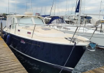 Blue and white motor yacht moored at a wooden dock, tied with a heavy rope, with other sailboats in the marina under a cloudy sky
