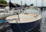 Motorboat docked at a marina with a dark blue hull and beige deck, tied to a wooden dock with ropes in calm water.