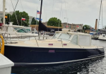 Blue motor yacht docked at a marina with other boats and flags in the background.