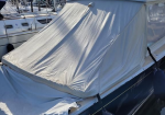 Powerboat at a marina covered with a white canvas cockpit cover; blue fenders along the hull and sailboats moored in the background.
