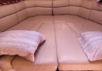 Top-down view of a beige leather sectional with padded back cushions forming a corner, two pastel striped pillows at the ends.